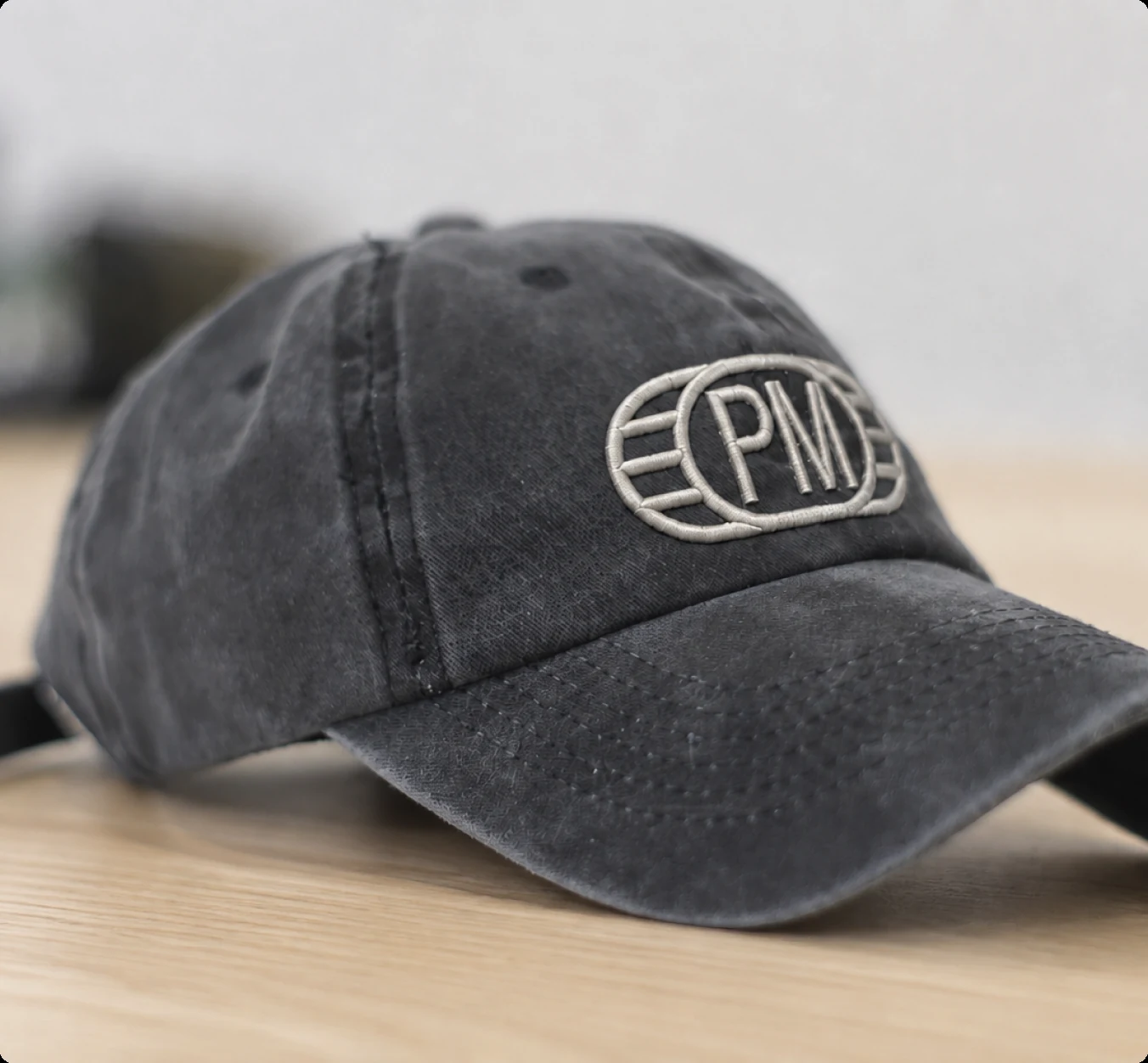 Washed-black cap embroidered with the PM monogram, on a wooden desk